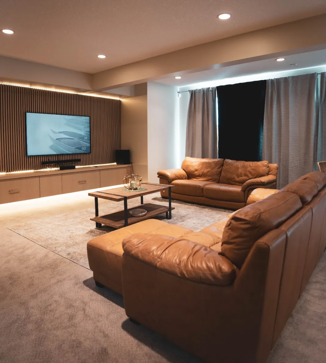 Finished basement living room with leather sofas, a wall-mounted television on a wood slat feature wall and pot lights